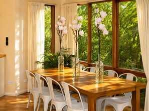 A dining area with a wooden table, white chairs, and three glass vases with branches and pink flowers.