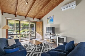 A living room with a wooden ceiling, a television on a stand, and a large window with a view of greenery.