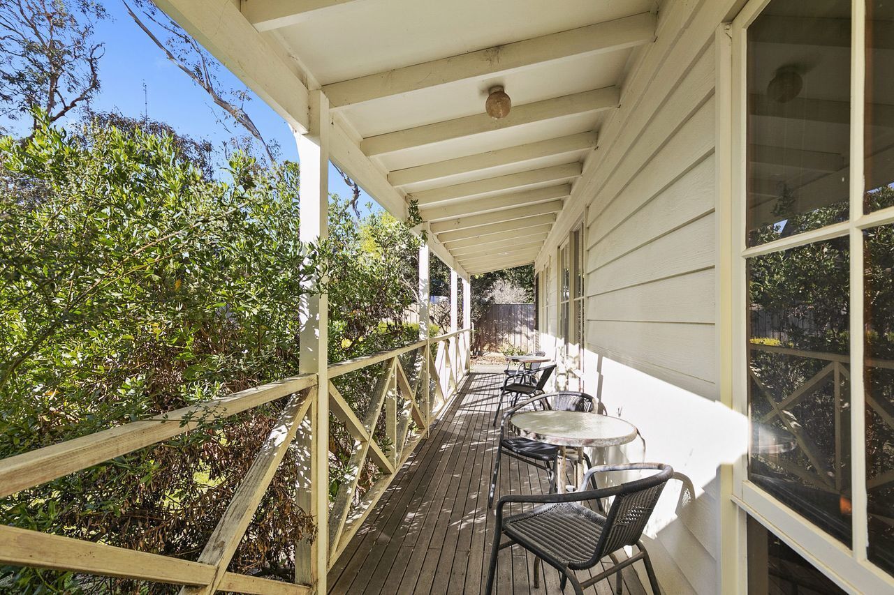 A covered outdoor patio with wooden railings, a table, and chairs.