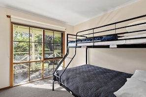 A bunk bed with a patterned mattress, a window with a view of greenery, and a sliding glass door.