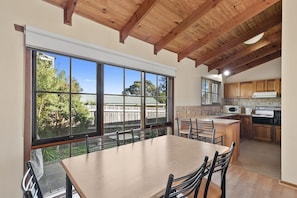 A modern kitchen with large windows, a dining area, and wooden ceiling beams.