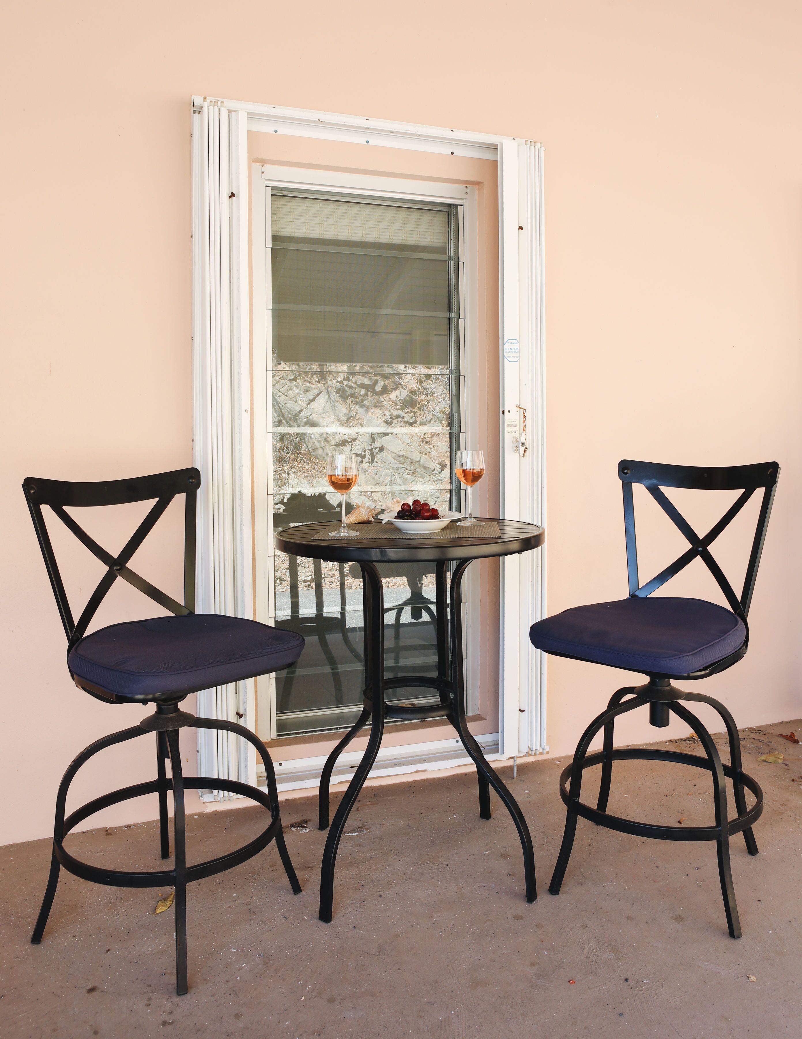 A small outdoor seating area with two chairs and a table, a glass door, and a view of a rocky landscape.