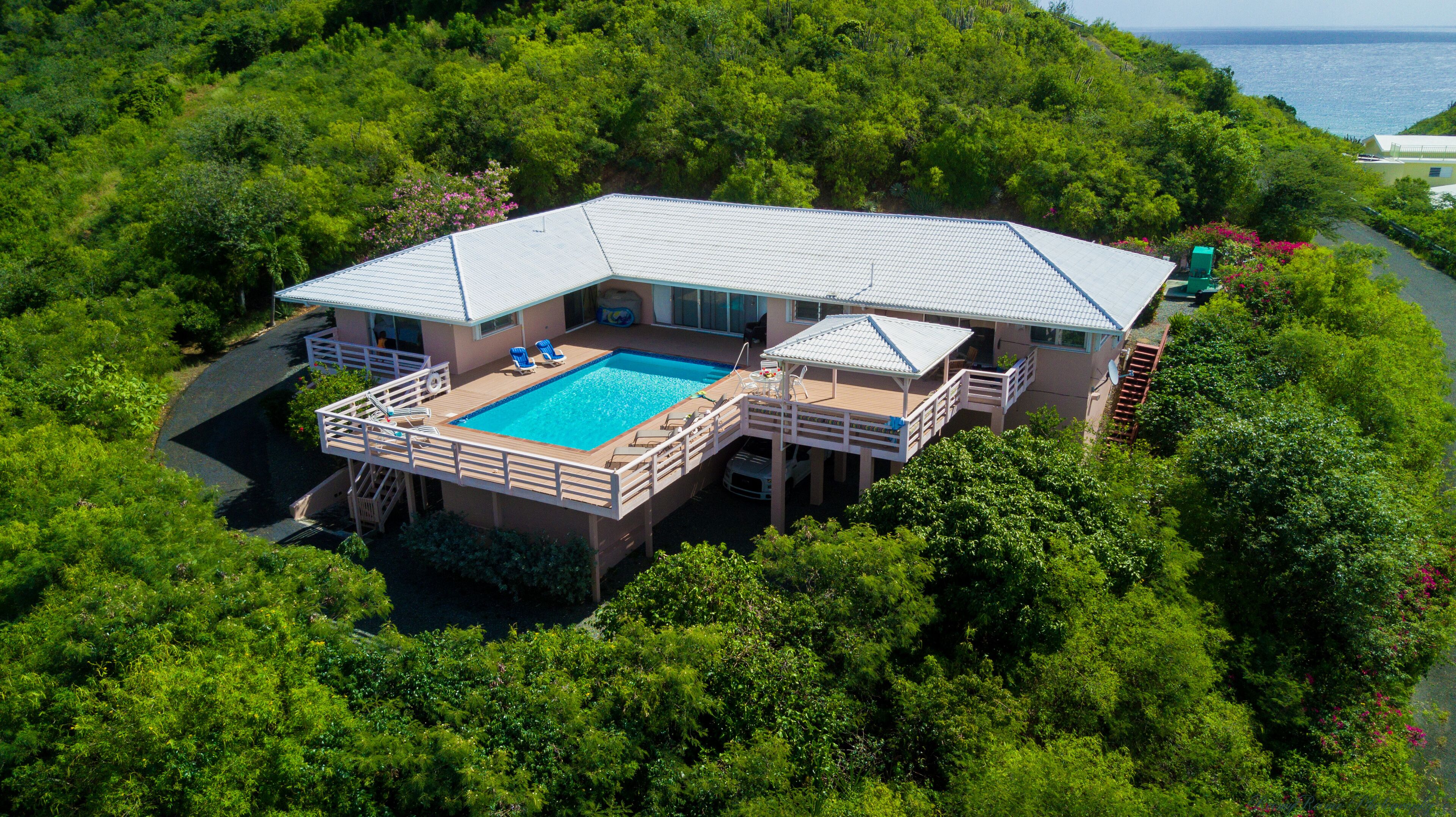 A large house with a swimming pool, surrounded by dense greenery and overlooking a body of water.