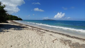 A sandy beach with gentle waves, a clear sky, and a distant island. - Paradise Awaits (Christiansted)