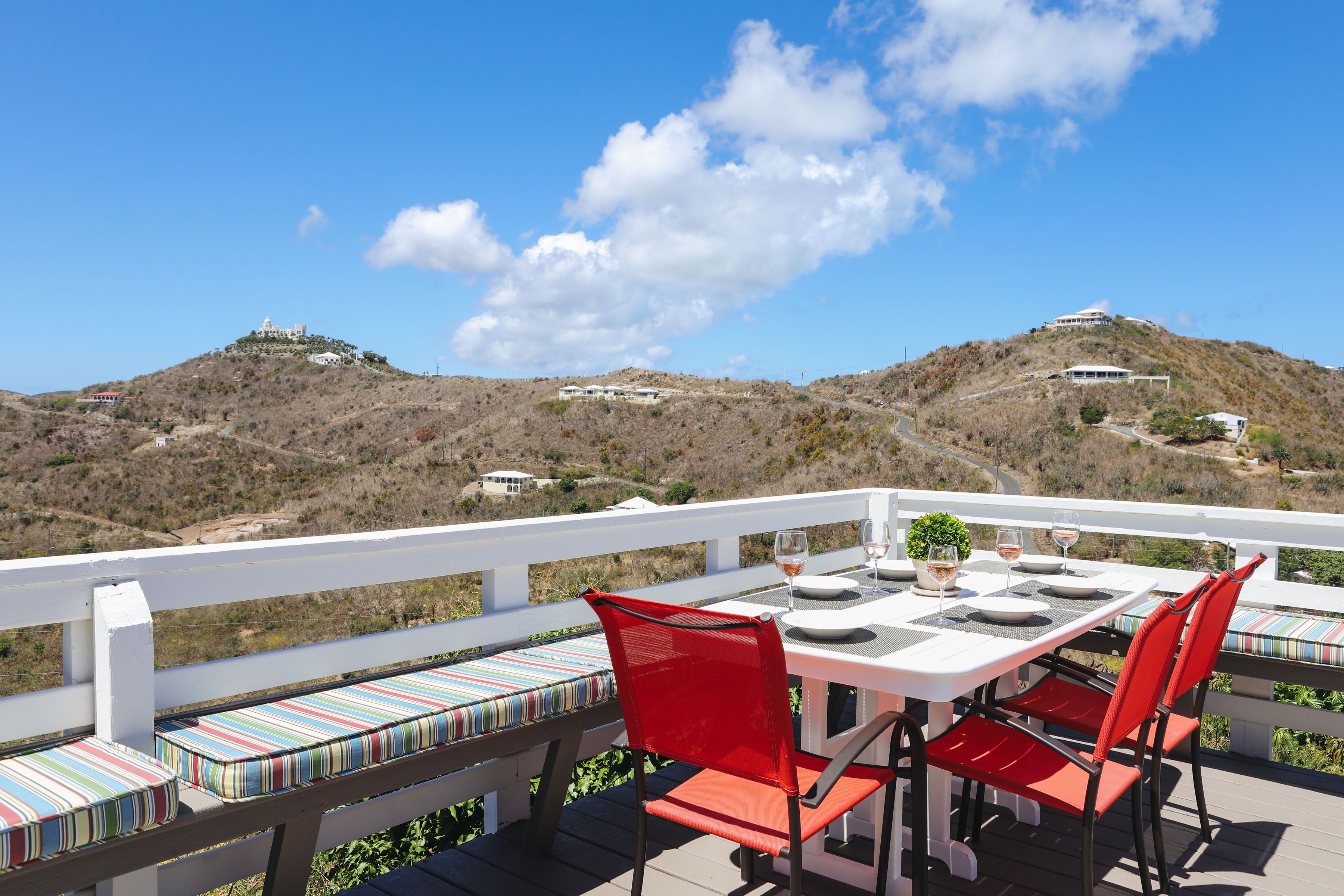 Eine Terrasse mit Esstisch, roten Stühlen und einem weißen Geländer.