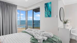 A bedroom with a bed, a view of the sea, a painting, and a plant.