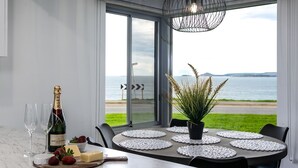 A dining area with a table set for two, a bottle of champagne, strawberries, cheese, and a potted plant.