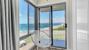 A balcony with a white chair, a view of the ocean, and a clear sky.