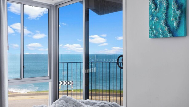 A room with a large sliding glass door leading to a balcony with a view of the sea.