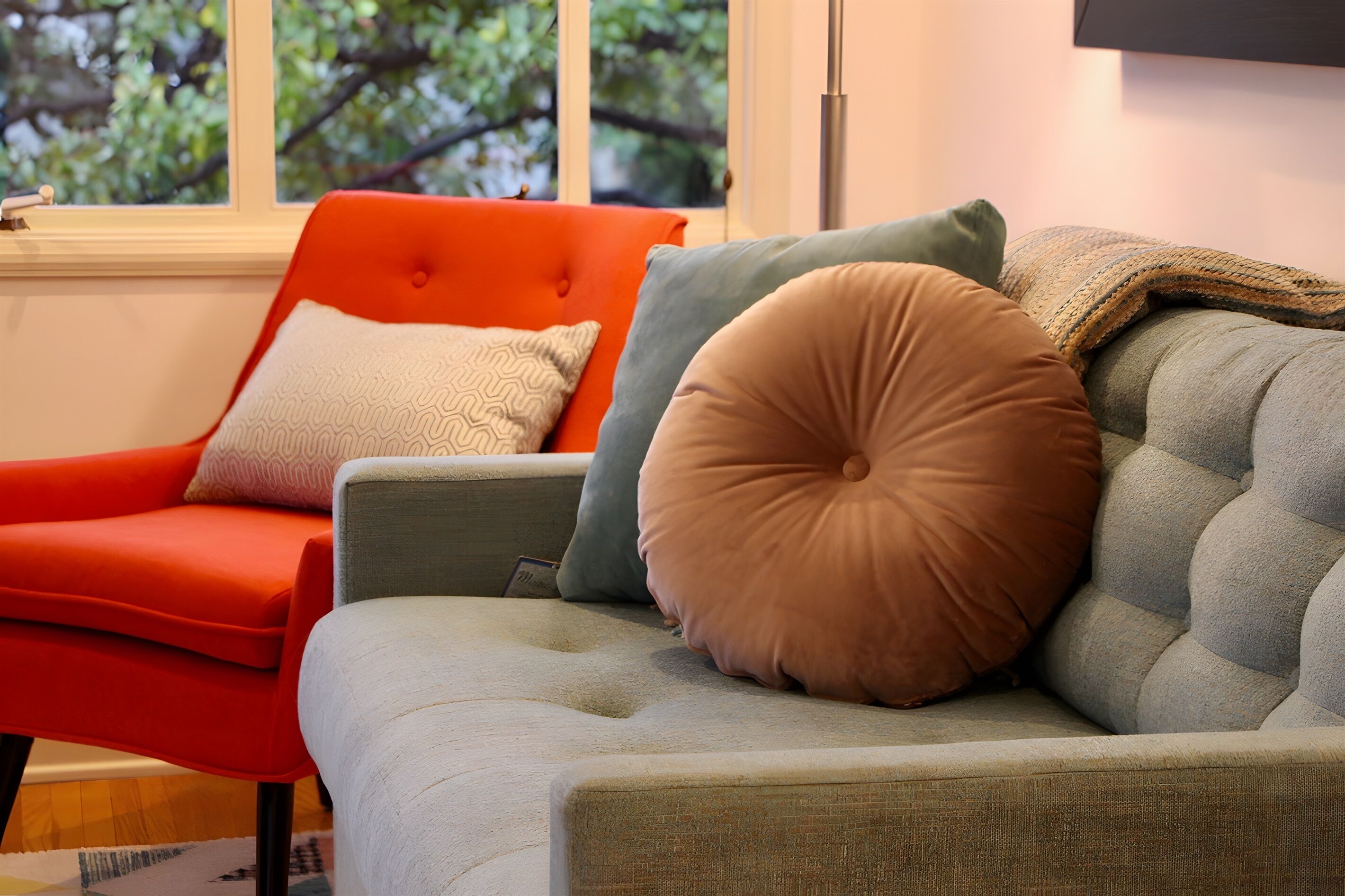 Una sala de estar moderna con un sofá gris y un sillón naranja, ambos con almohadones decorativos.