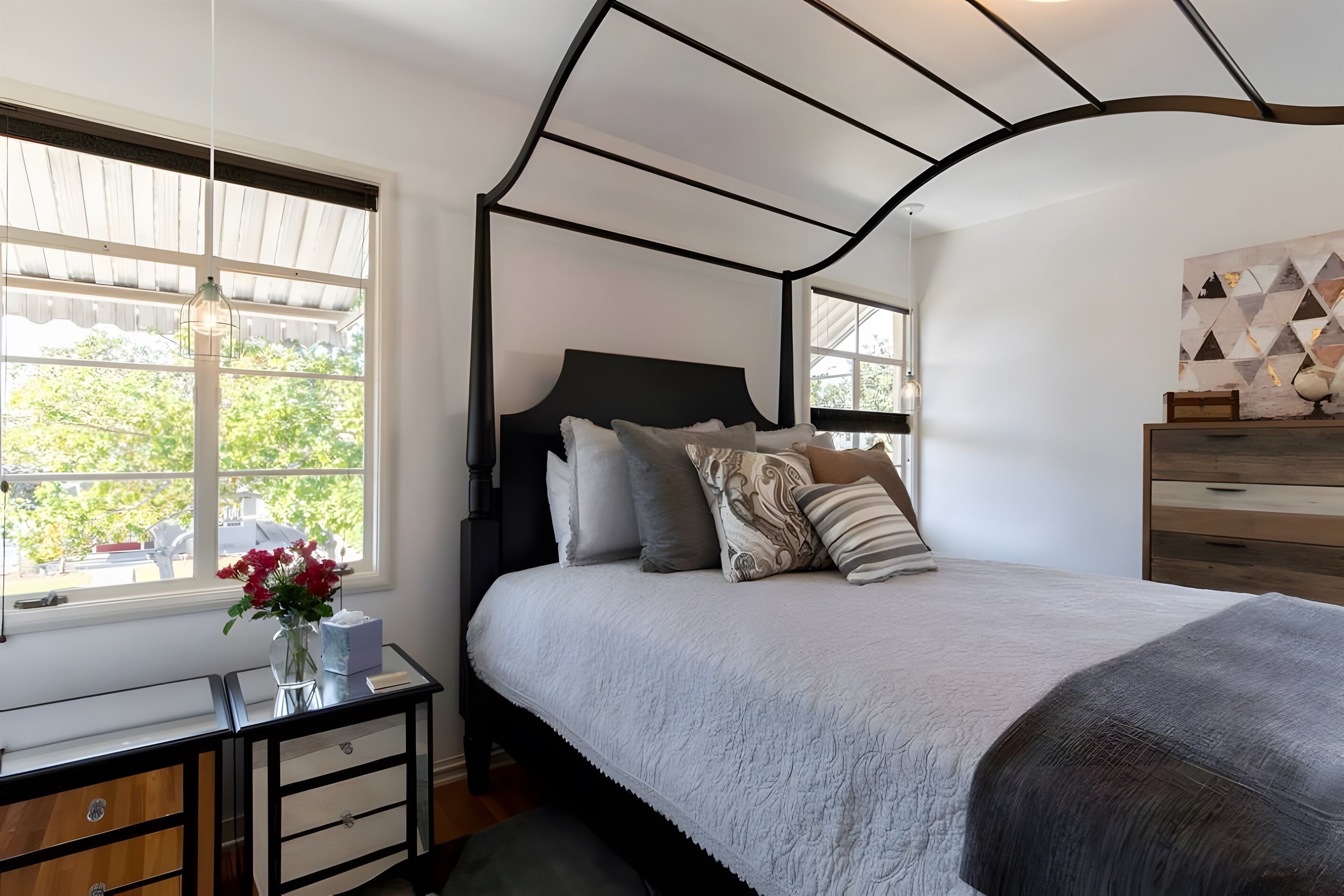 Een slaapkamer met een hemelbed, een nachtkastje met een bloevas en een kast met lades.