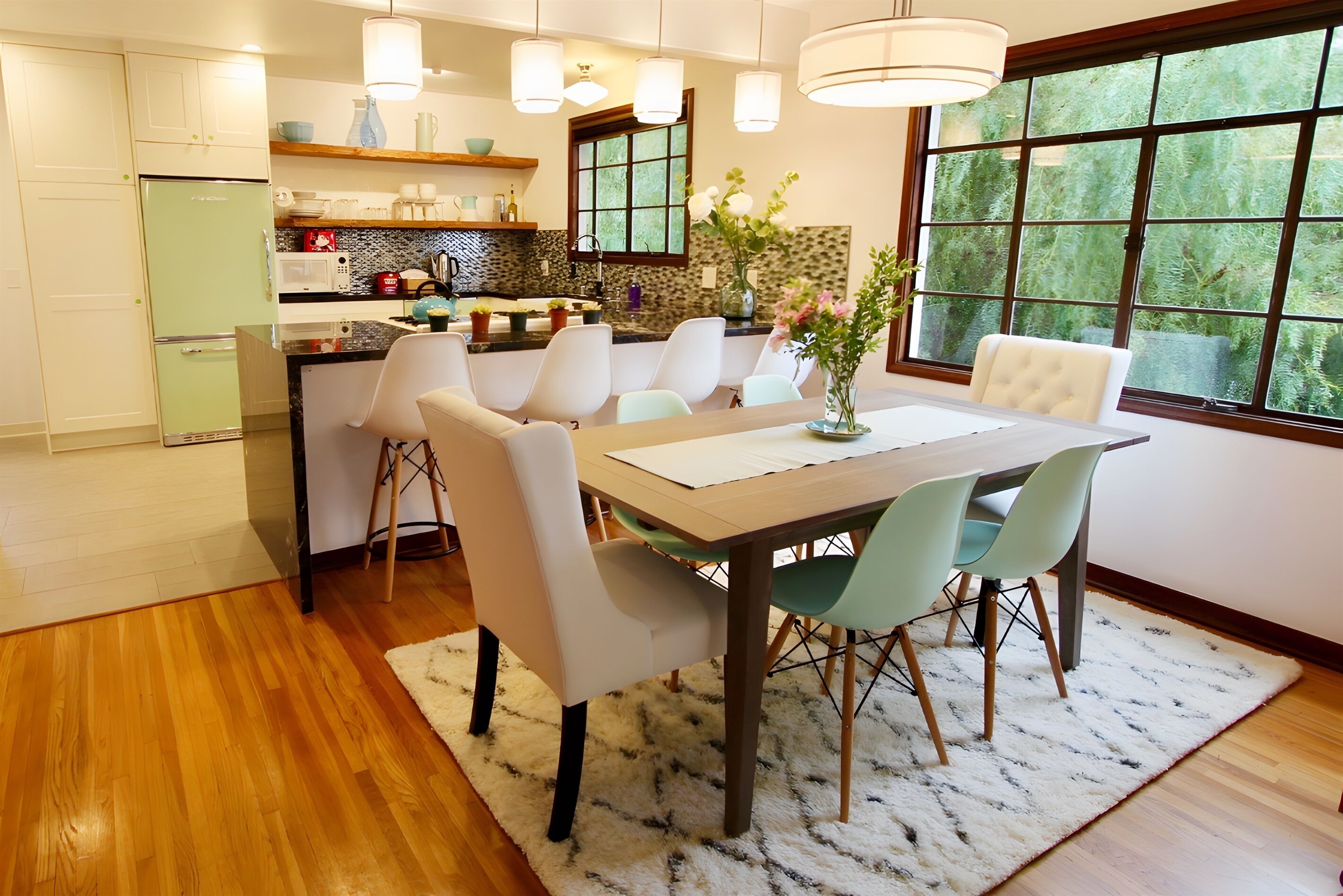 A modern kitchen with a dining area, wooden flooring, and large windows.