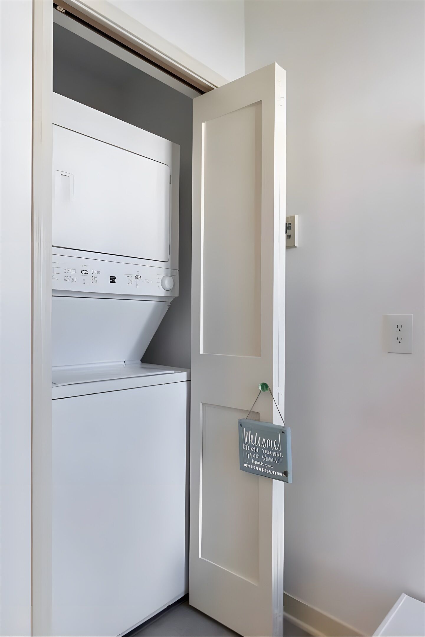 Une buanderie avec un lave-linge et un sèche-linge blancs, un panneau d’accueil et un interrupteur sur le mur.
