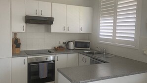 A kitchen with white cabinets, a microwave, a kettle, and a sink.