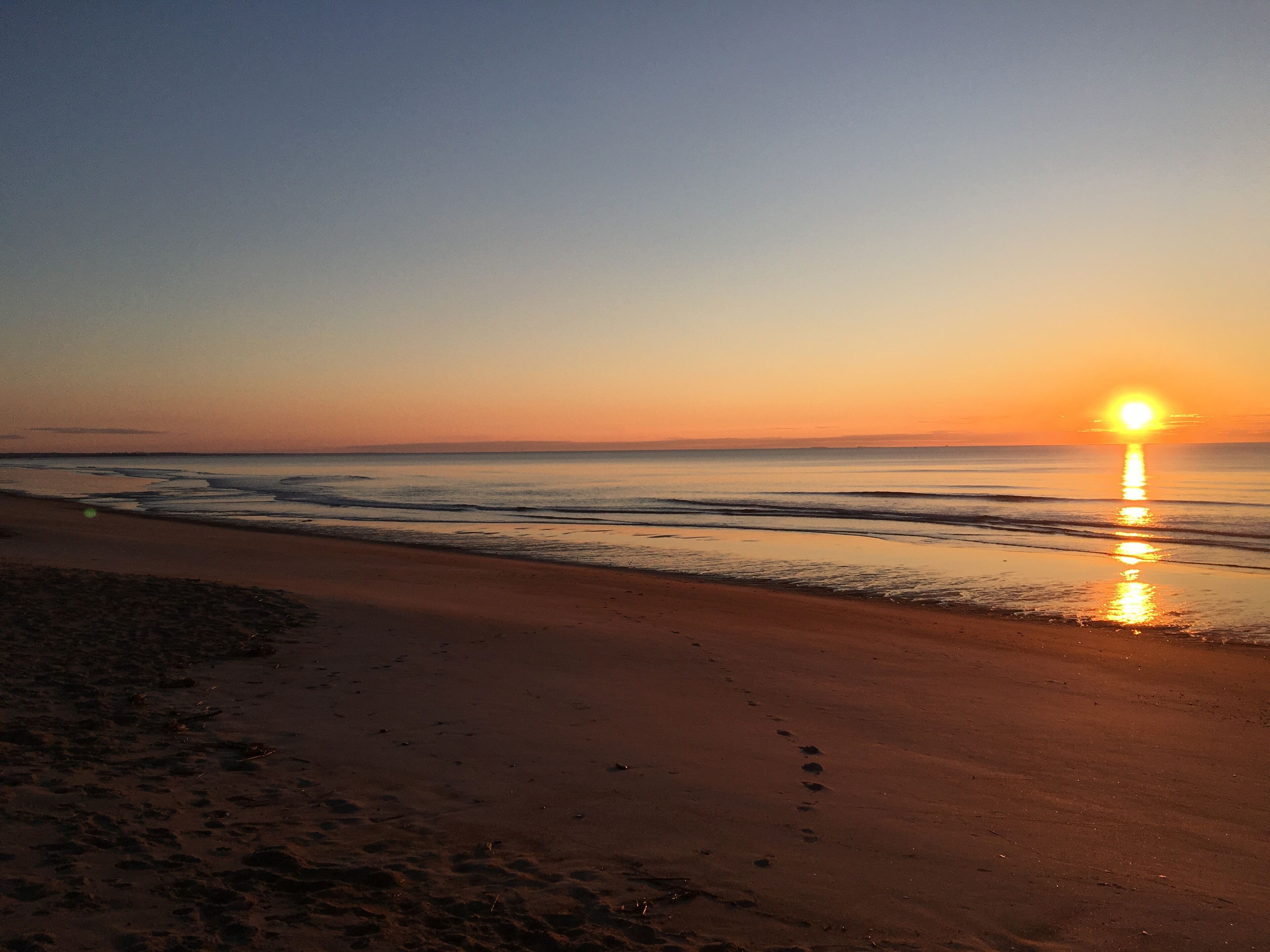 A beach at sunset with the sun reflecting on the water.