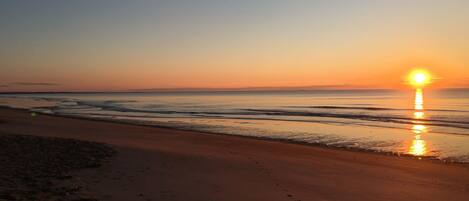 A beach at sunset with the sun reflecting on the water.