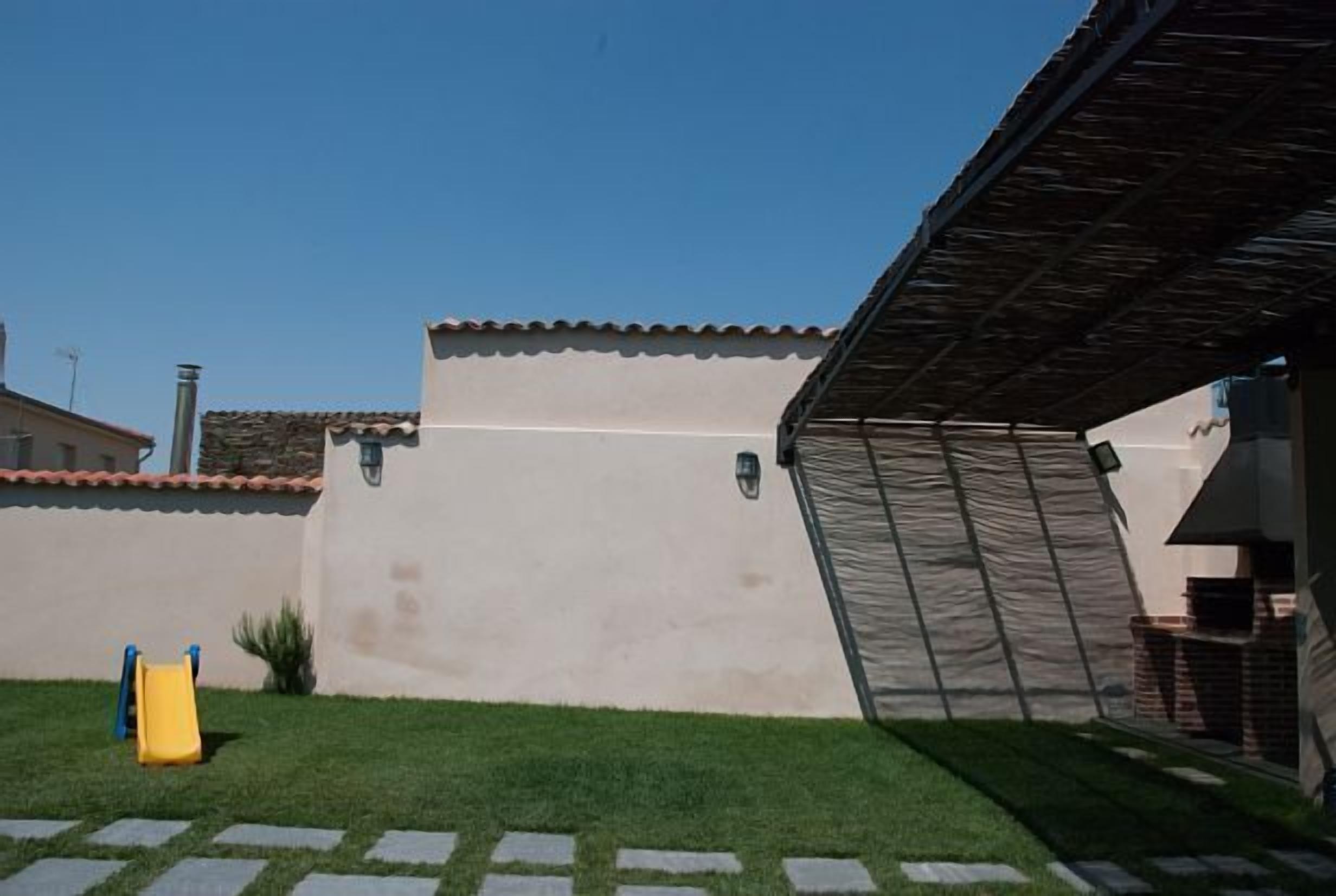 Un cortile con uno scivolo giallo, un pergolato e un edificio con tetto in tegole.
