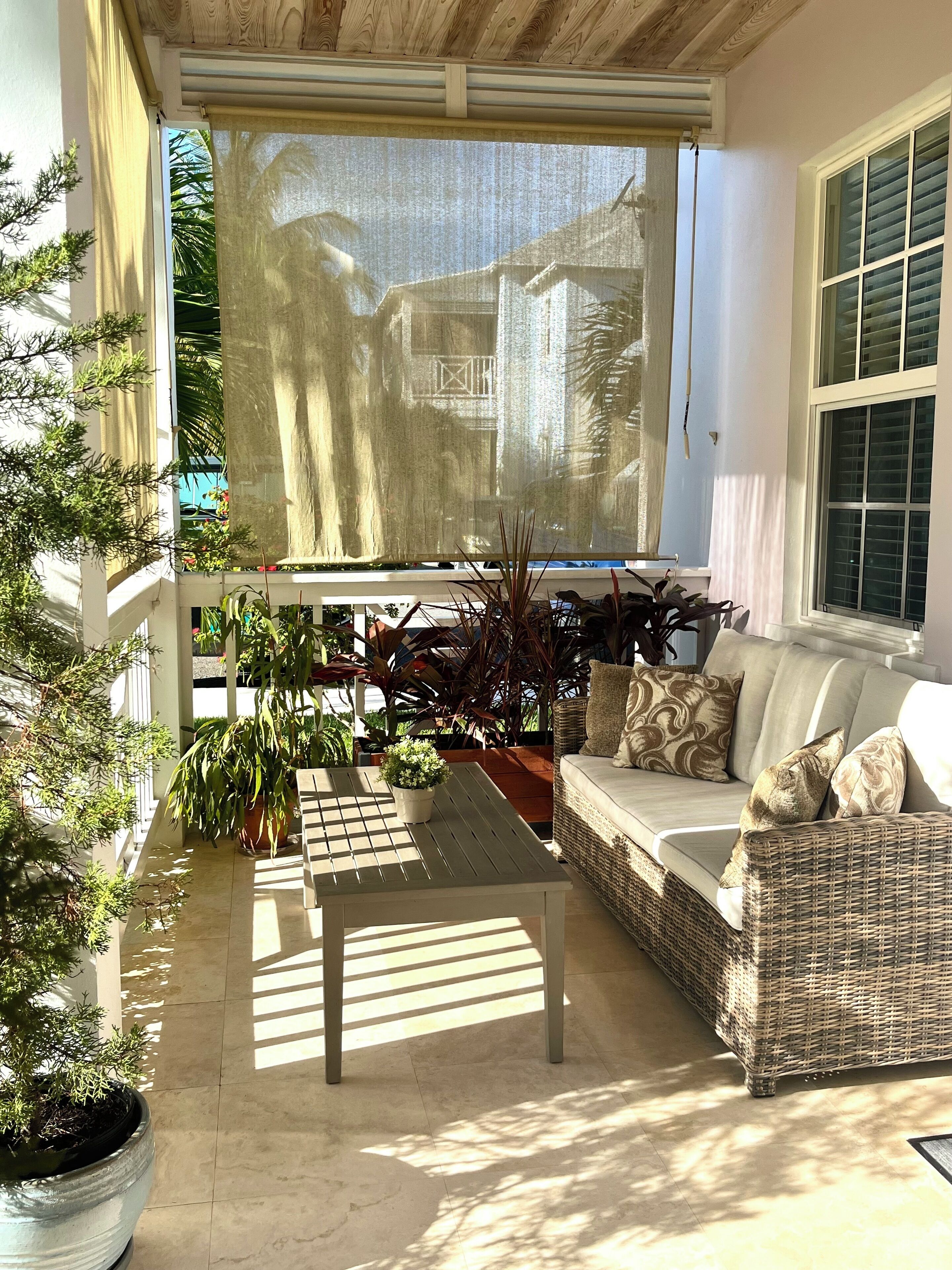 Un patio ensoleillé avec un canapé en osier, une petite table et des plantes en pot.