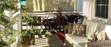 Un patio ensoleillé avec un canapé en osier, une petite table et des plantes en pot.