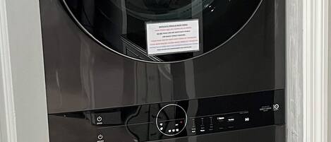 Lavadora LG ThinQ negra con panel de control y mensaje que indica limpiar el filtro de pelusas antes y después de cada ciclo.