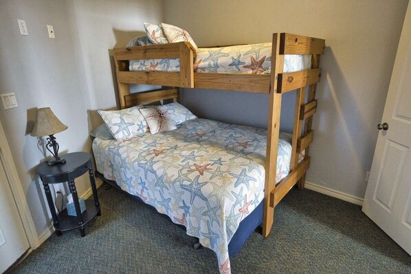 A bunk bed with a starfish-patterned bedspread, a small side table with a lamp, and a door in the background.