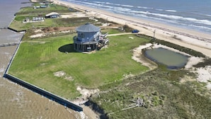 Una propiedad costera con un edificio circular grande, un estanque pequeño y una playa al fondo.
