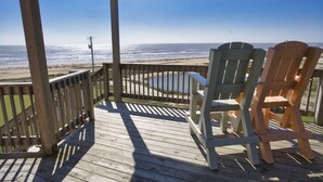 Una terraza de madera con dos sillas Adirondack que dan a una playa.