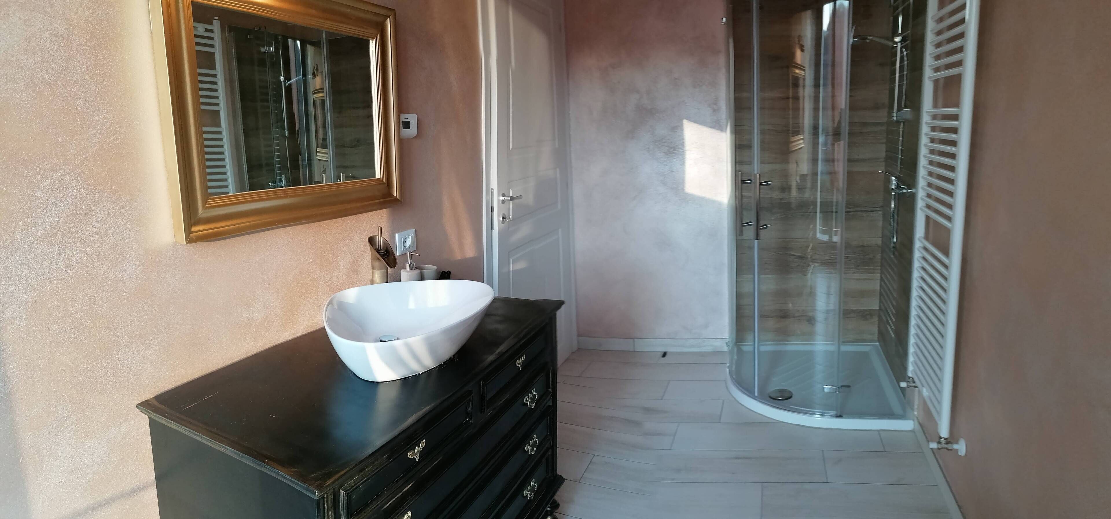 Een badkamer met een witte wastafel, een spiegel en een douche met glazen wanden.