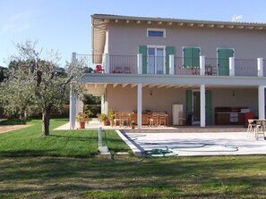 Una casa de dos pisos con un porche cubierto, mobiliario de exterior y un jardín.