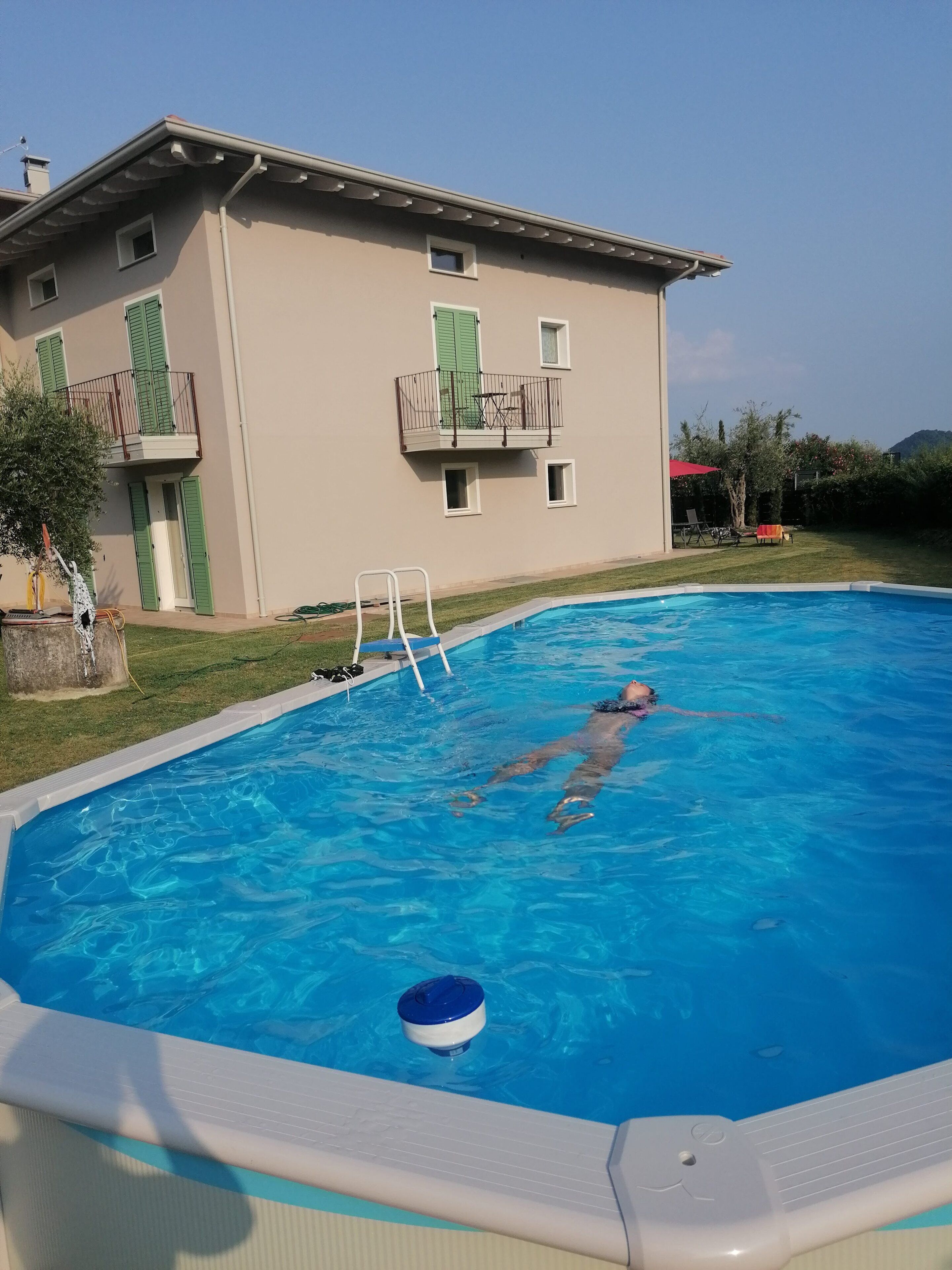 Une piscine dans laquelle une personne nage, un escalier de piscine et, au fond, un bâtiment doté de balcons.