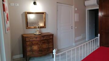 Quarto com guarda-roupa de madeira, penteadeira com gavetas, cama com colcha vermelha, mesa de cabeceira com abajur e espelho fixado na parede.