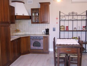 Cuina amb armaris de fusta, forn integrat, cafetera i prestatge metàl·lic amb objectes decoratius.