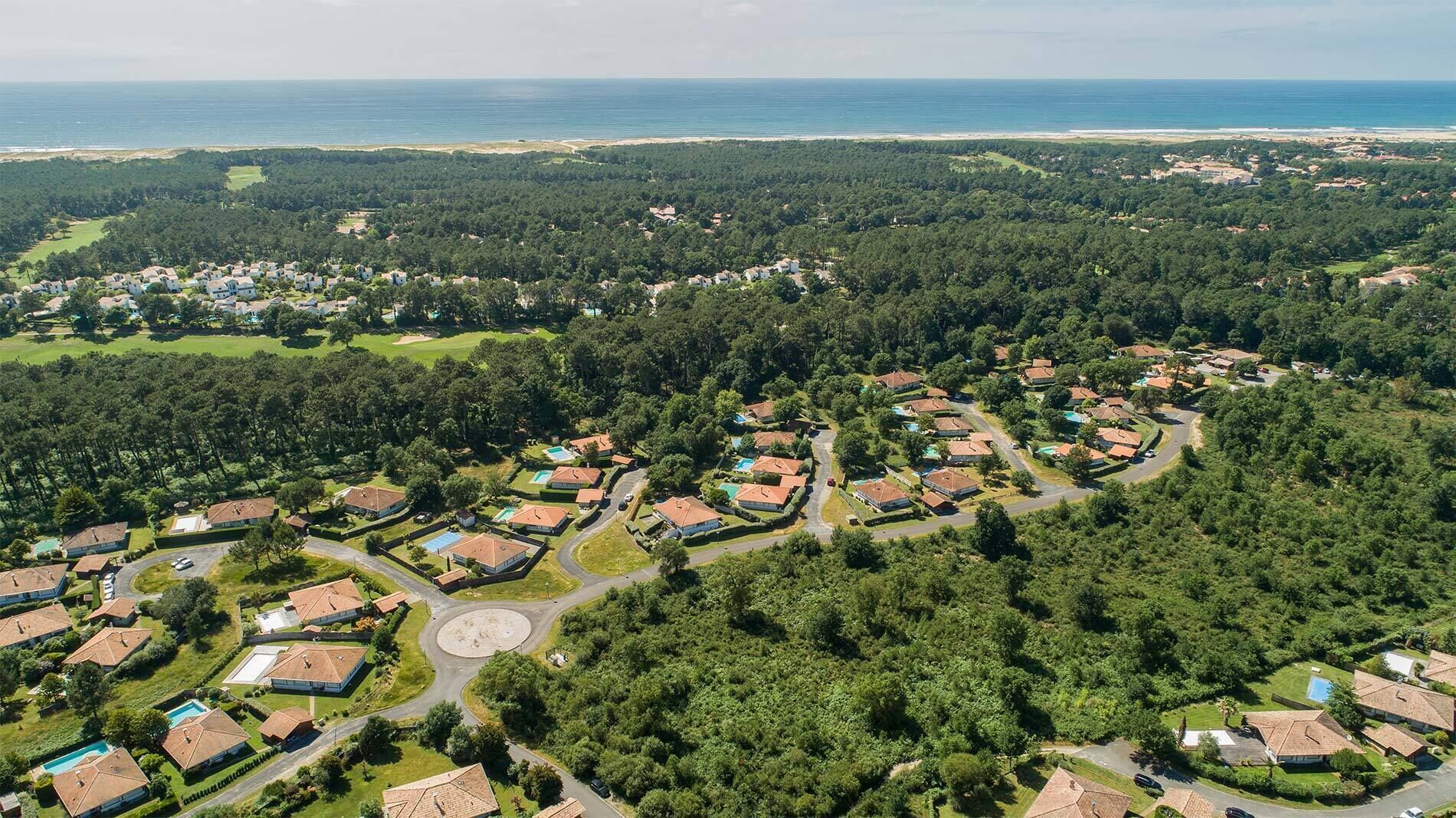 Une vue aérienne d’un quartier résidentiel avec des maisons, des routes et une plage en arrière-plan.