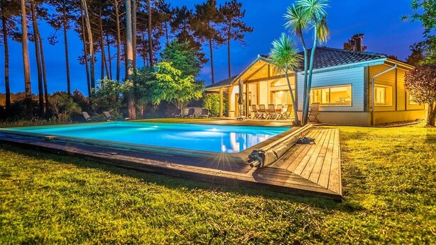Une maison avec une piscine, entourée d’arbres et dotée d’un patio bien éclairé.