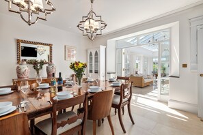 A dining room with a large wooden table set for six, surrounded by chairs. There is a chandelier above the table and a large mirror on the wall. - Coedrath House - Luxury Manor, Swim Spa, Sea Views (Saundersfoot)