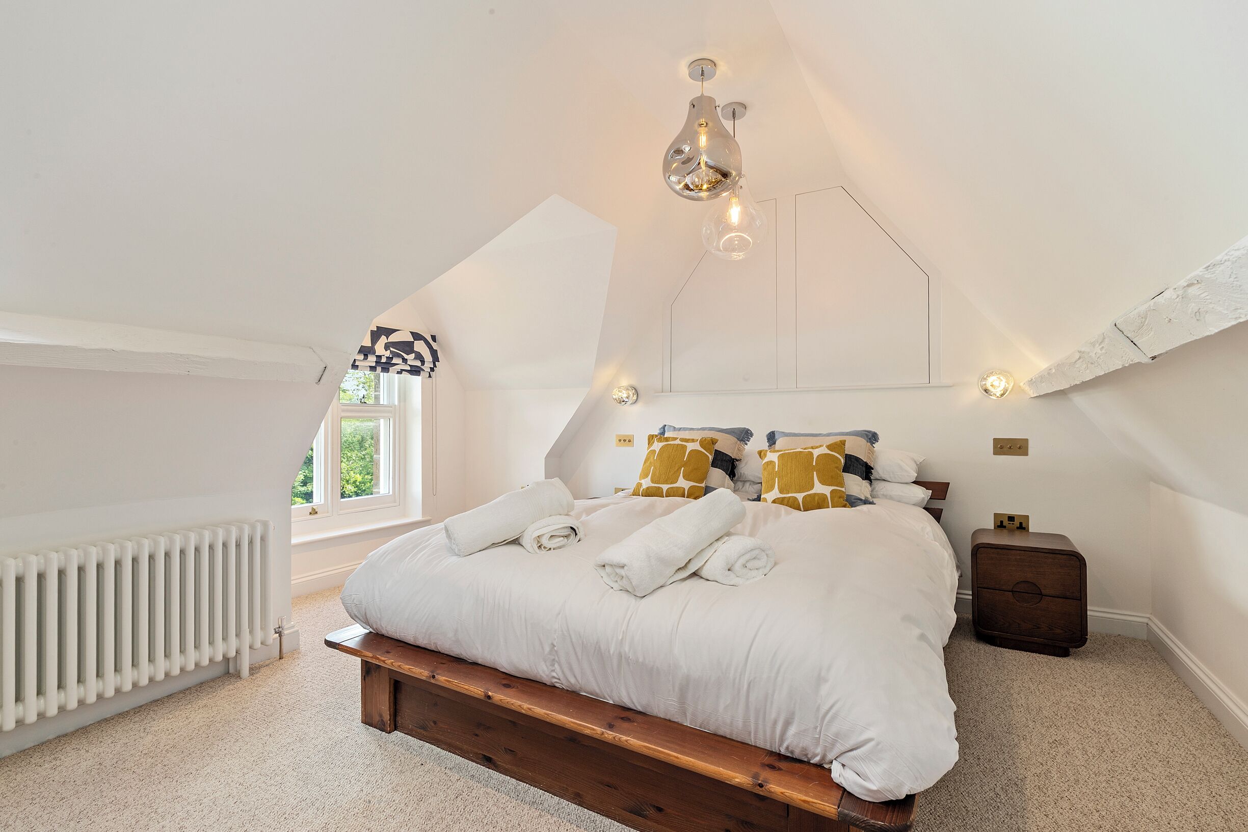 Une chambre avec un plafond en pente, un cadre de lit en bois, du linge de lit blanc et un radiateur.
