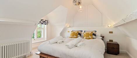 A bedroom with a sloped ceiling, a wooden bed frame, white bedding, and a radiator.