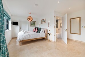 A bedroom with a bed, a television, a door, and a bathroom visible through an open door. - Coedrath House - Luxury Manor, Swim Spa, Sea Views (Saundersfoot)