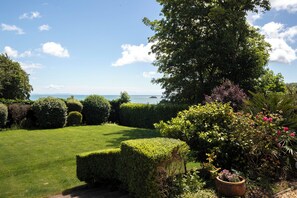 A well-maintained garden with neatly trimmed hedges, a variety of shrubs, and a view of the sea. - Coedrath House - Luxury Manor, Swim Spa, Sea Views (Saundersfoot)