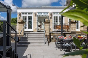 A building with a staircase leading to a door, outdoor seating with tables and chairs, and a clear sky. - Coedrath House - Luxury Manor, Swim Spa, Sea Views (Saundersfoot)