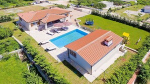 Une propriété résidentielle dotée d’une piscine, de deux maisons aux toits recouverts de tuiles rouges et d’une pelouse bien entretenue.