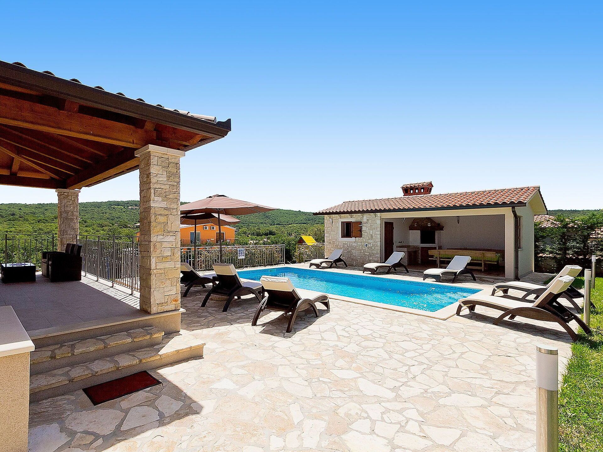A pool area with stone flooring, lounge chairs, and a covered seating area.