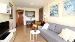 Ein Wohnzimmer mit grauem Sofa, einem kleinen weißen Tisch und einem Fernseher auf einer weißen Kommode.