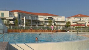 A swimming pool with a clear blue water, surrounded by a wooden fence and a building with a red roof in the background. - Luxurious Beach Apartment, Juan Les Pins (Antibes)