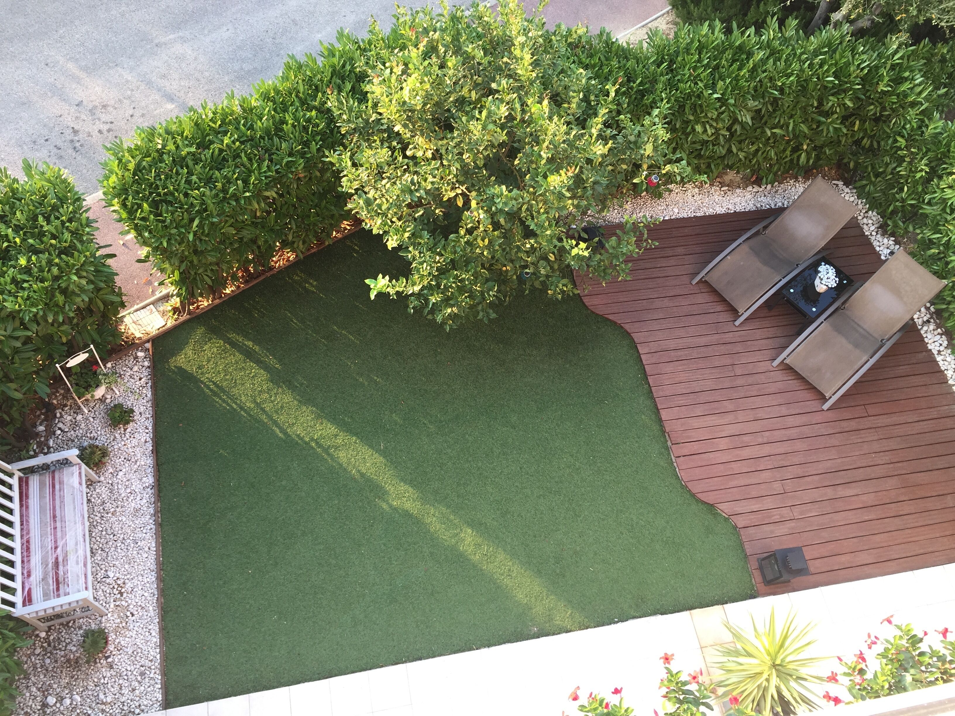 A rooftop garden with a wooden deck, a seating area with a table and chairs, and a variety of plants and trees.