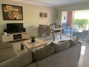 Una sala moderna con televisor de pantalla plana, una mesa de centro con una planta, un sofá y un comedor con sillas y una mesa.
