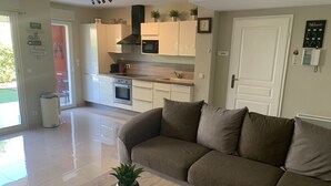 A modern kitchen with white cabinets, a built-in oven, microwave, and a stainless steel range hood. There is a beige sofa in the living area with a small table and a potted plant. - Luxurious Beach Apartment, Juan Les Pins (Antibes)