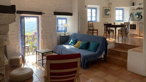 Ein gemütliches Wohnzimmer mit einer Couch, einem Esstisch und Stühlen. Es gibt eine Küchenzeile mit einem Herd und Schränken.