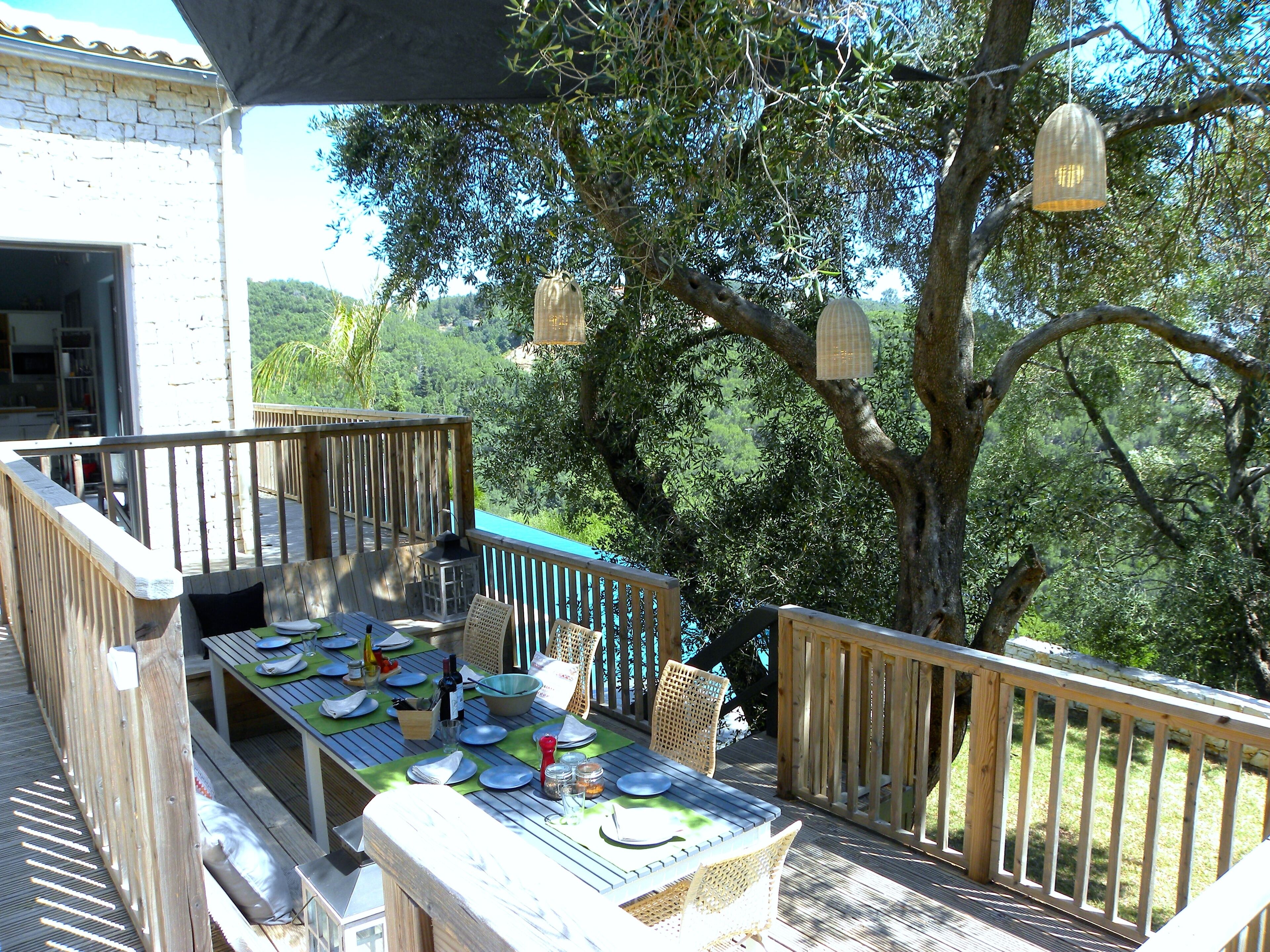 An outdoor dining area with a wooden deck, a table set for a meal, and a view of the surrounding greenery.