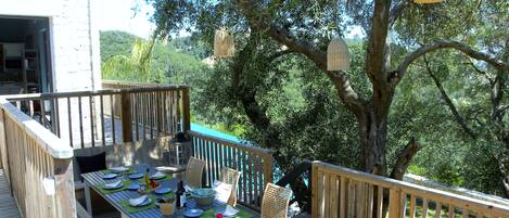 An outdoor dining area with a wooden deck, a table set for a meal, and a view of the surrounding greenery.